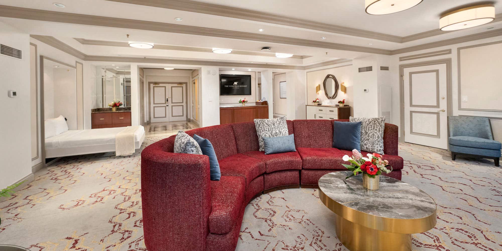 A wide shot of a luxurious, remodeled hotel suite, showing a wet bar with bar stools and multiple, elegant seating areas.