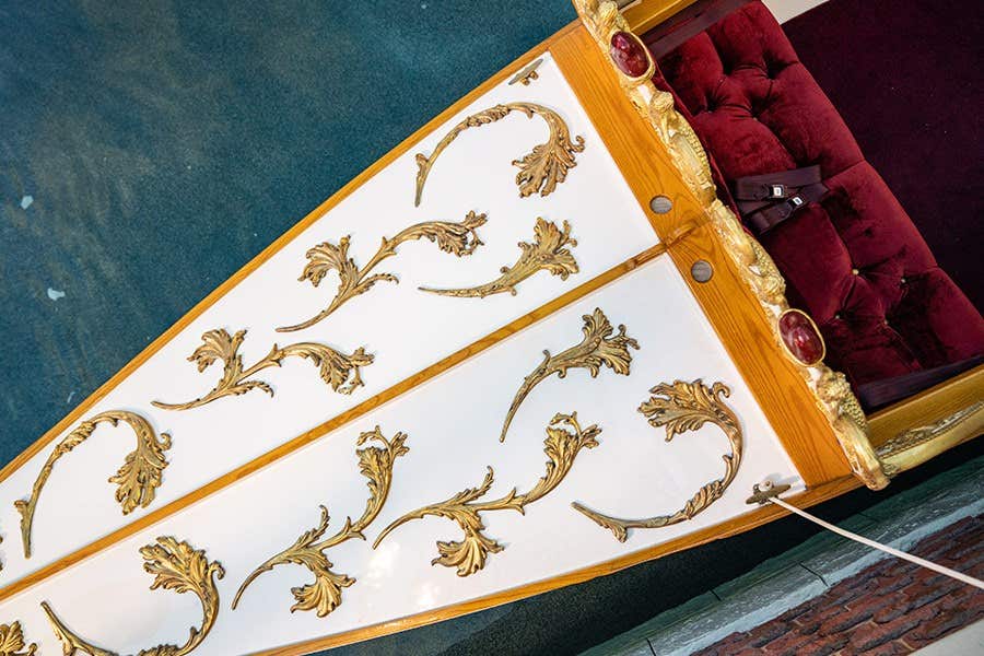 Ornate boat with gold floral patterns on the deck and a red cushioned seat viewed from above.