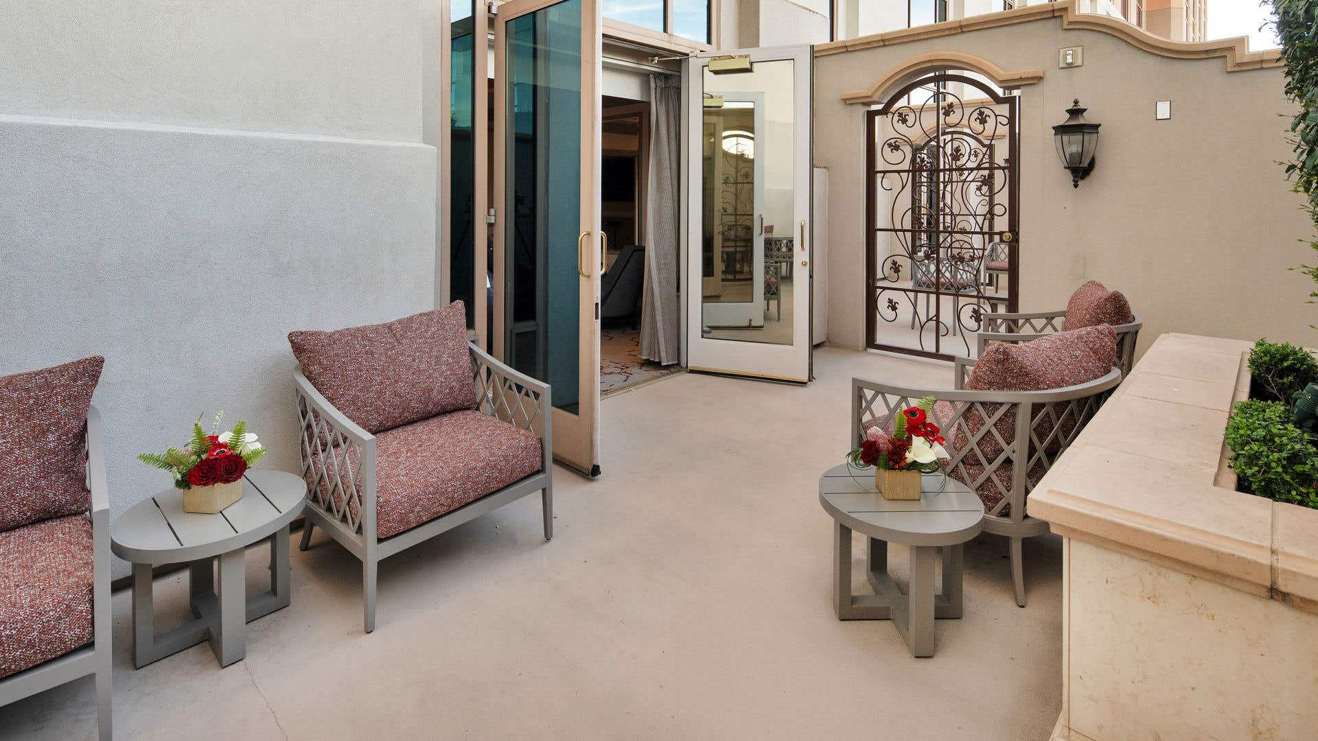 A hotel suite's private patio with comfortable, modern outdoor furniture, an ornate iron gate, and glass doors leading into the suite.