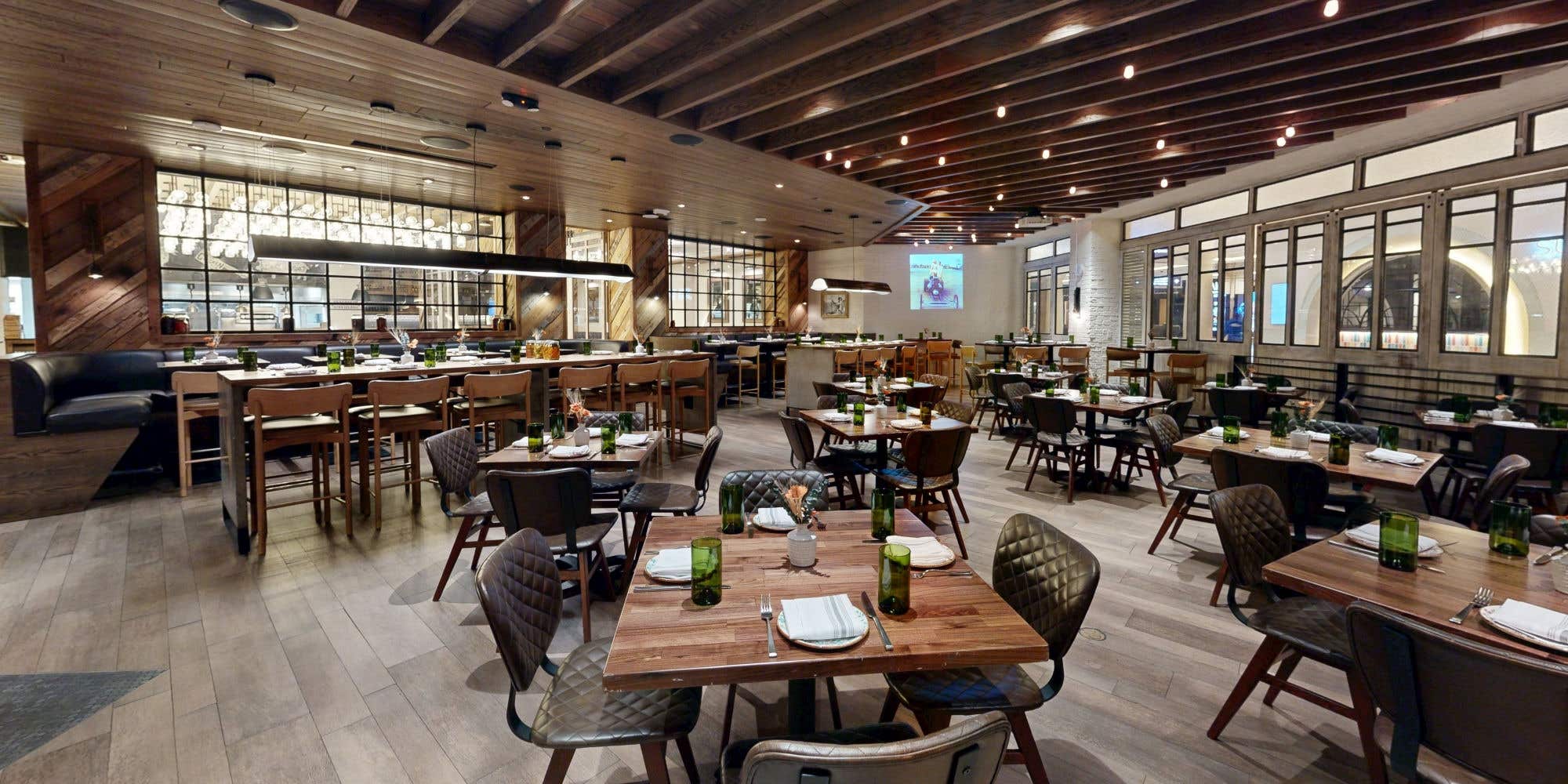 Warm, modern restaurant dining room with wood accents, set tables, and ambient lighting.