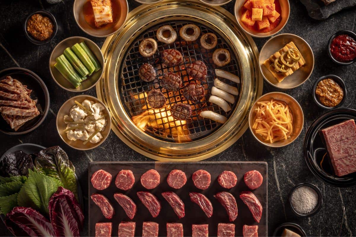 Raw cuts of meat and side dishes around a hibachi grill.