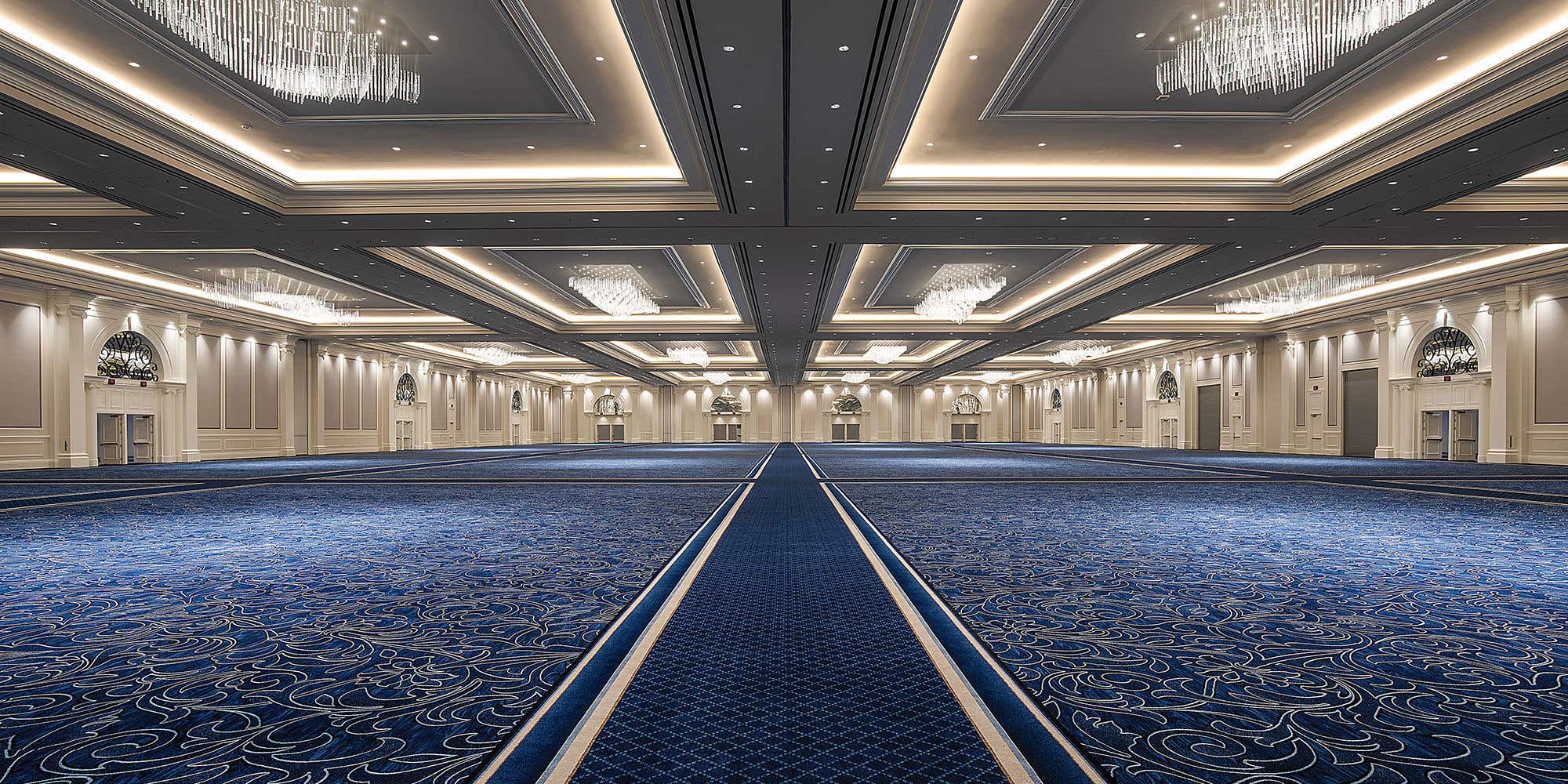 Venetian Ballroom with chandeliers, blue patterned carpet, and arched windows.