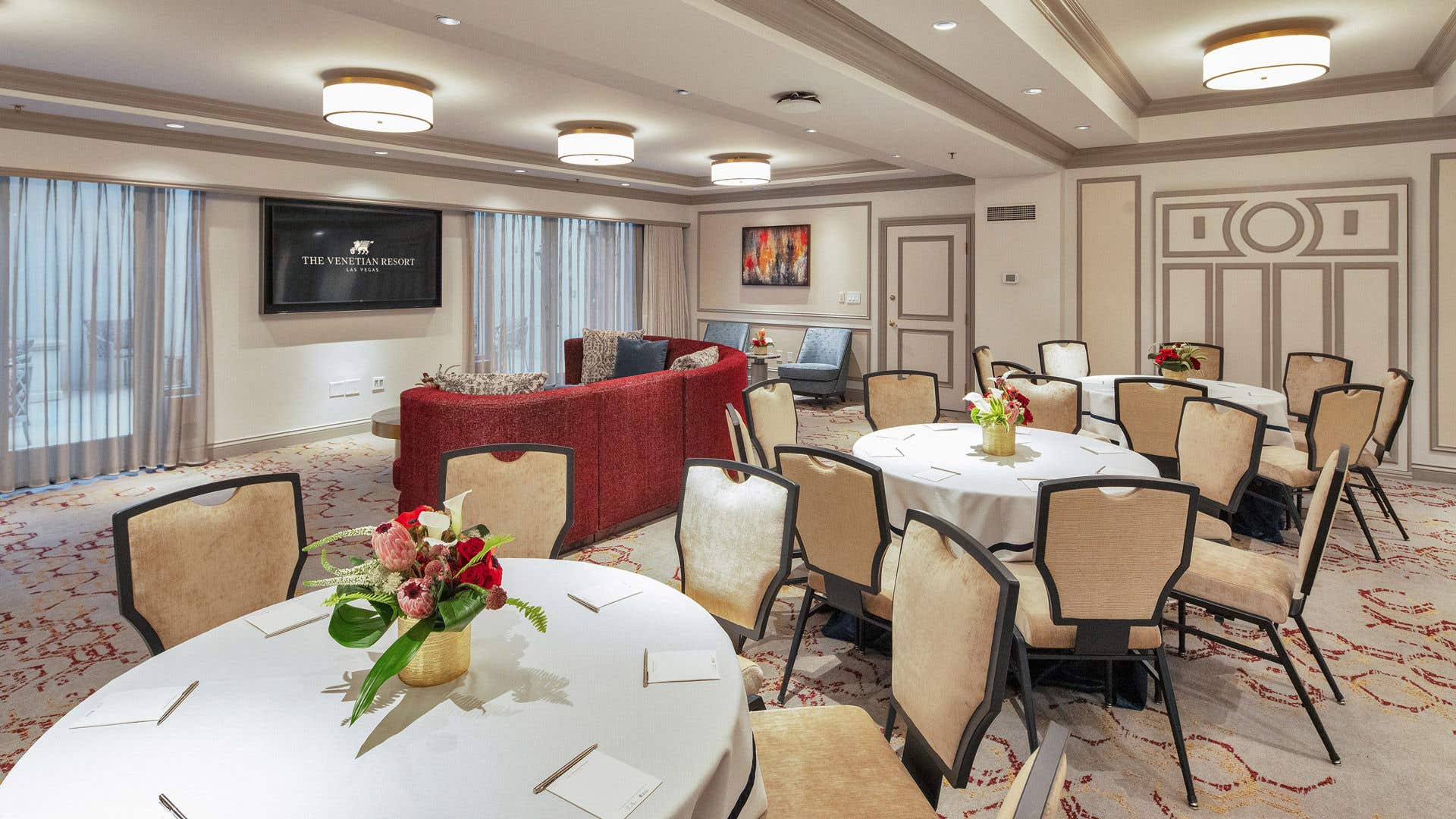 A newly remodeled hospitality parlor configured for a meeting, featuring round tables with white cloths and a comfortable lounge area in the back.